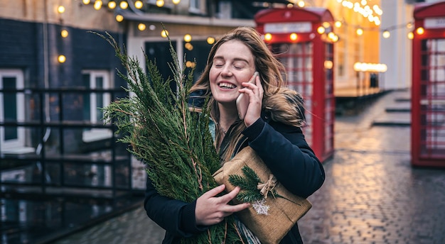 Una giovane donna con un albero di natale e una confezione regalo che parla al telefono