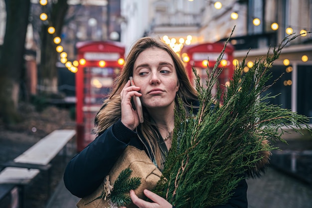 クリスマスツリーと電話で話しているギフトボックスを持つ若い女性