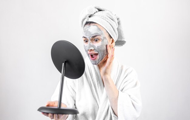 Young woman with a clay mask on her face in front of a mirror