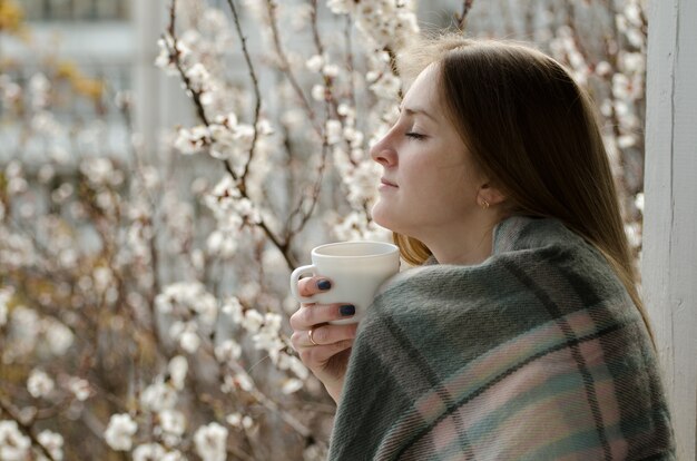 目を閉じて、春を楽しむお茶のカップを持つ若い女性