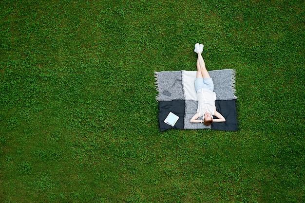 Молодая женщина с закрытыми глазами, лежа на одеяле на зеленой траве