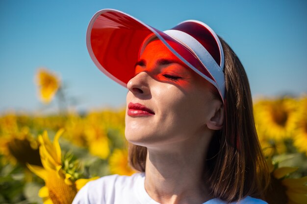 young woman with closed eyes in red sun visor and white t-shirt looks at the sky