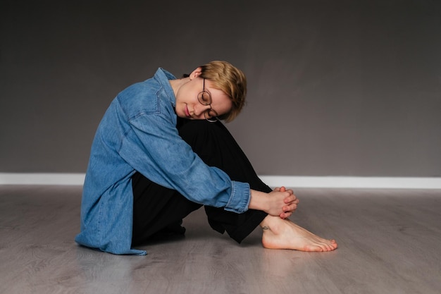 Foto giovane donna con gli occhi chiusi e i capelli corti seduta sul pavimento che medita all'interno ragazza che fa esercizio di yoga in studio