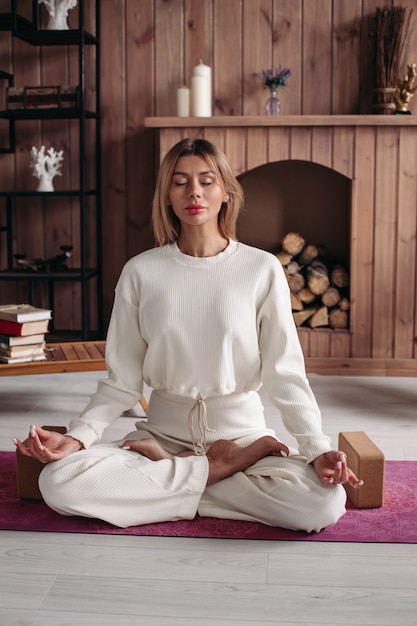 Young woman with closed eyes sitting on the rug and meditating in the room. Healthy and lifestyle concept