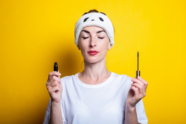 Young woman with closed eyes in white shirt holding a mascara 