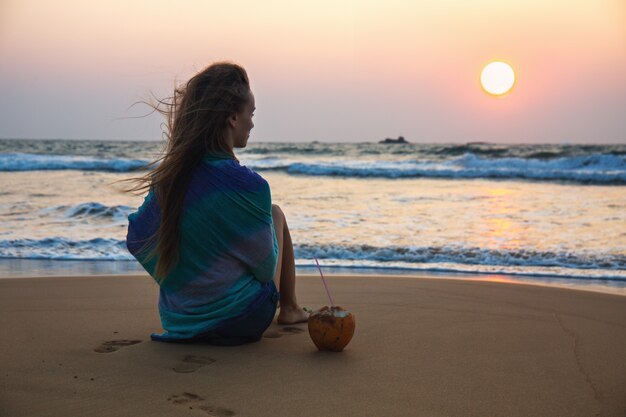 Young woman with a coconut looks at the sunset