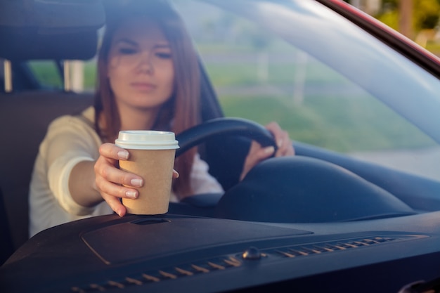 車のホイールの後ろに手でコーヒーを持つ若い女性