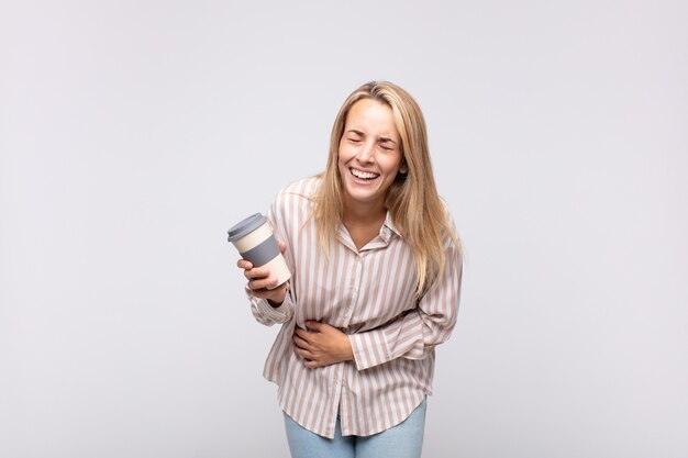 Giovane donna con un caffè che ride ad alta voce a uno scherzo esilarante, si sente felice e allegra, si diverte