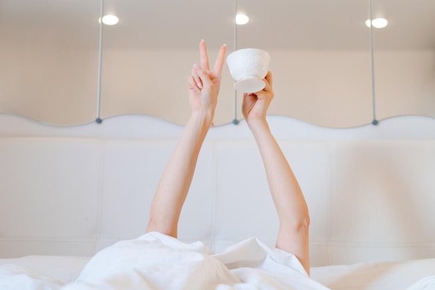 Young woman with a coffee mug in bed with white linens Minimal happy morning