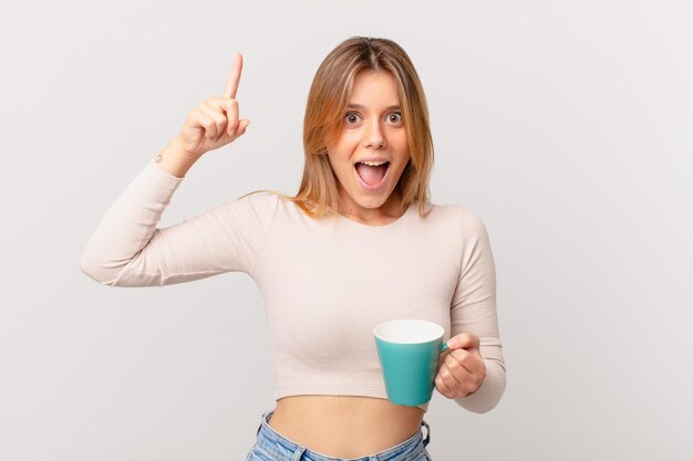 Young woman with a coffee mug feeling like a happy and excited genius after realizing an idea