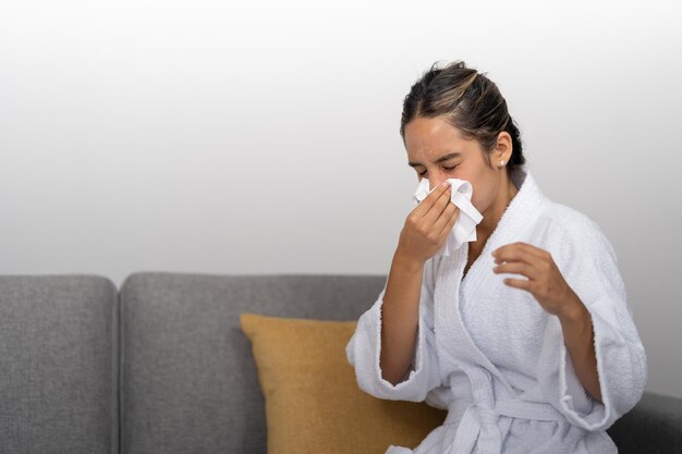 Young woman with a cold blowing her nose with a piece of tissue paper