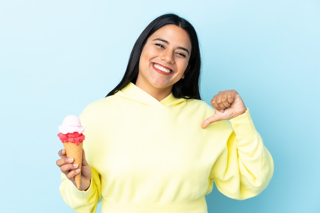 Young woman with a cornet ice cream on blue wall proud and self-satisfied