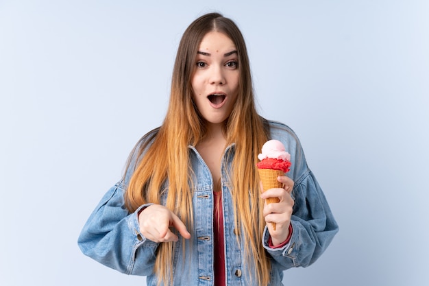 Foto giovane donna con un gelato della cornetta isolato sulla parete blu sorpresa e indicando parte anteriore