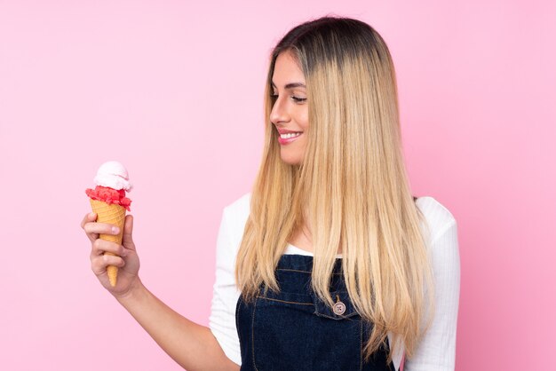 Young woman with a cornet ice cream over isolated pink wall with happy expression