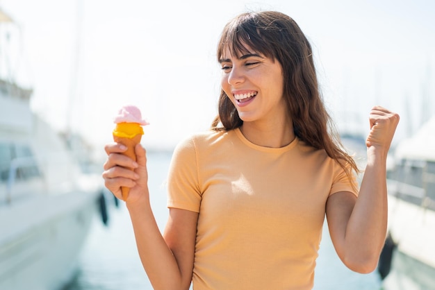 屋外で勝利を祝うコルネットアイスクリームを持つ若い女性