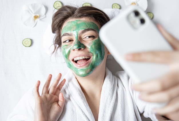 La giovane donna con una maschera cosmetica sul viso fa un selfie su uno smartphone