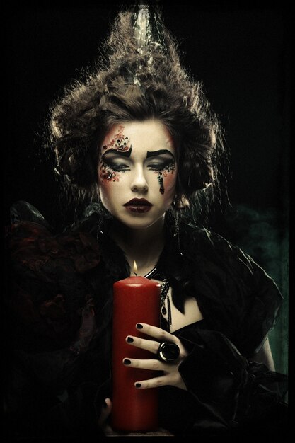 Молодая женщина с творческим макияжем держит свечу. Тема Хэллоуина.