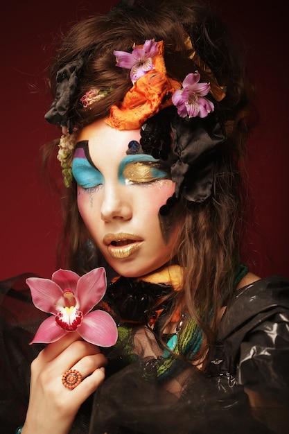 Young woman with creative make up holding pink flower