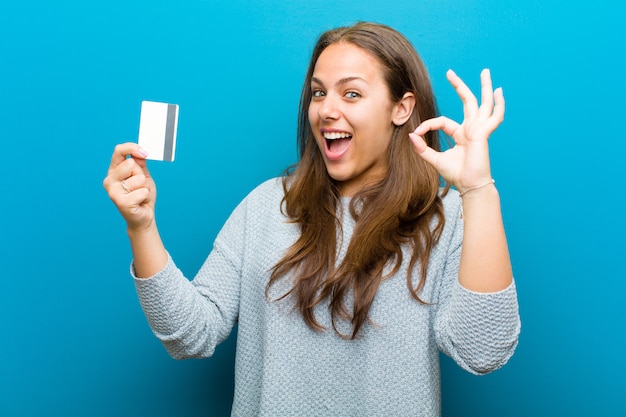Young woman with a credit card   blue wall
