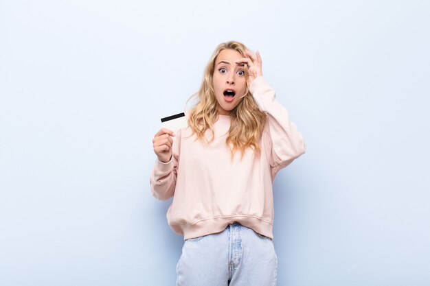 young woman with credit card looking happy astonished and surprised