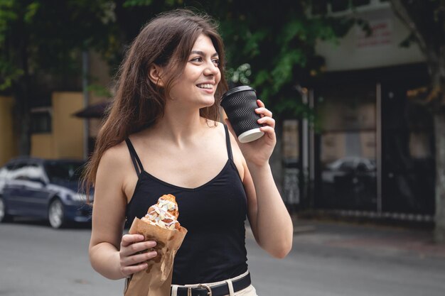 A young woman with a croissant and a cup of coffee on a city walk