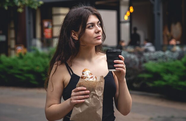 A young woman with a croissant and a cup of coffee on a city walk