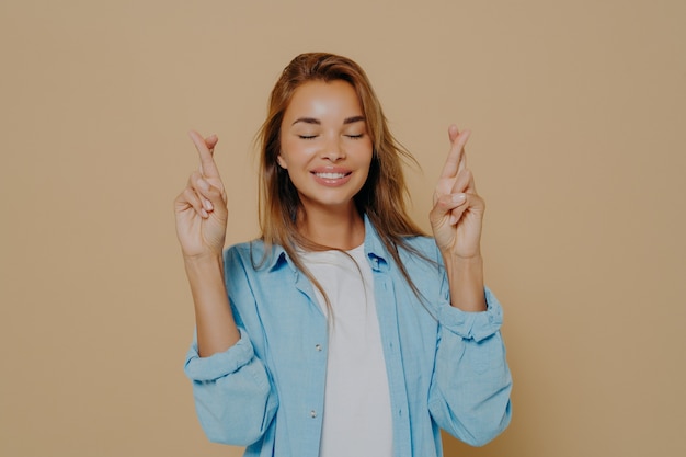 Young woman with crossed fingers on beige background