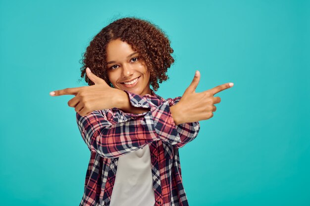 Young woman with crossed hands, blue wall, positive emotion. Face expression, female person looking on camera in studio, emotional concept, feelings