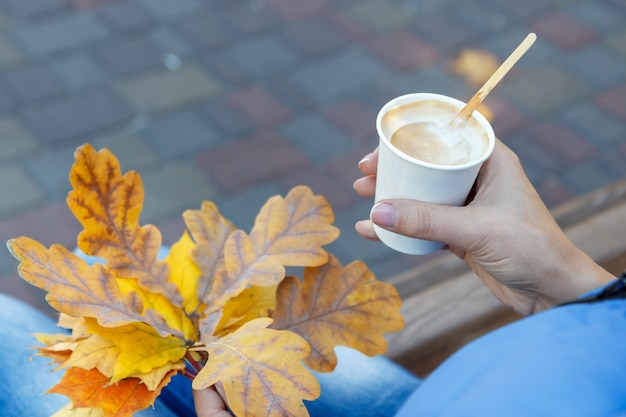 一杯のコーヒーと紅葉を持つ若い女性。