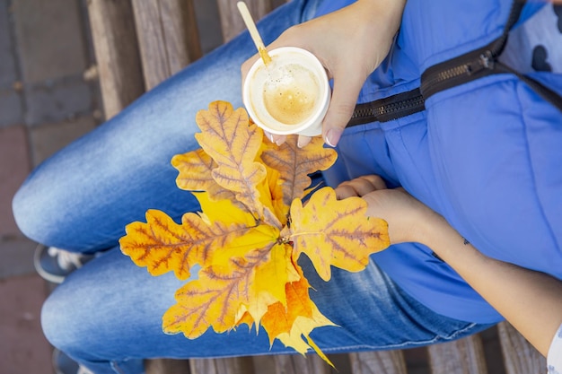 一杯のコーヒーと秋のカエデの葉を持つ若い女性