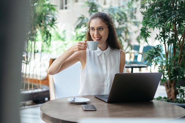 インターネットカフェに座っているコーヒーを飲みながら若い女性