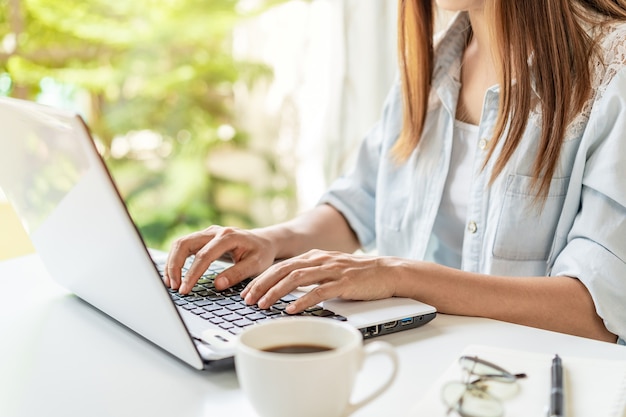 Young woman with cup of coffee sitting at living room and working on laptop at home