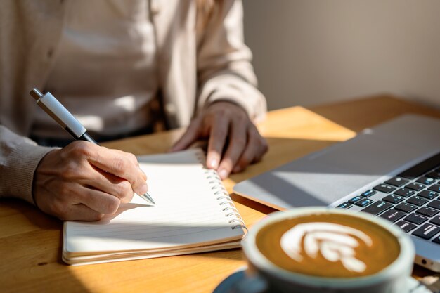 Giovane donna con una tazza di caffè seduta e che lavora al computer portatile al bar