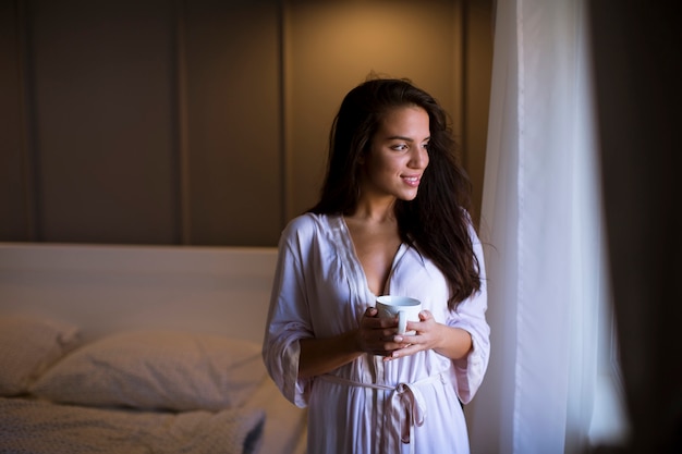 一杯のコーヒーや紅茶、窓のそばに立っている若い女性