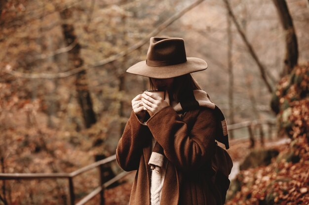 写真 秋の公園でコーヒーのカップを持つ若い女性