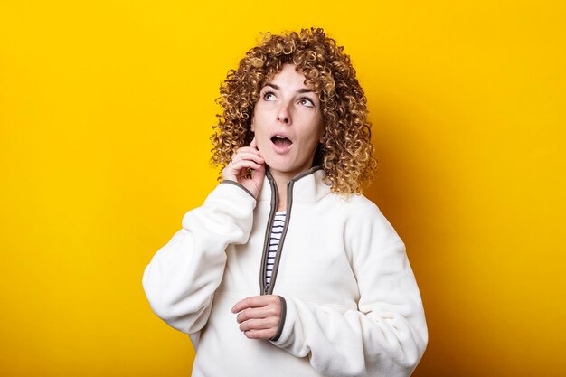 Young woman with curly African hair looks pensively up against a yellow background.