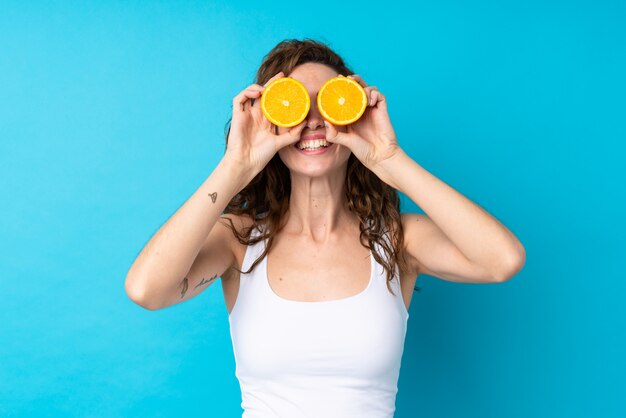 Young woman with curly hair holding an orange over isolated blue