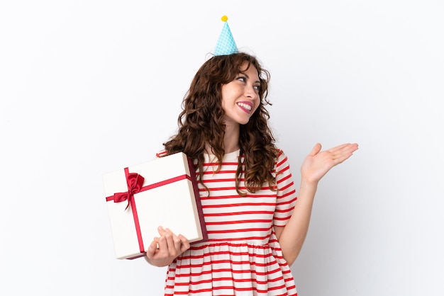 Young woman with curly hair holding present isolated on white background extending hands to the side for inviting to come
