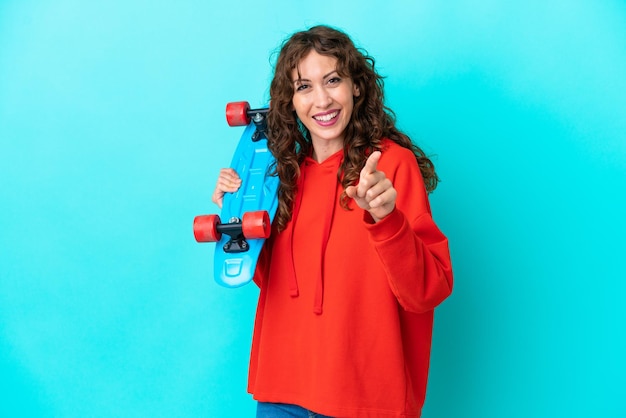 Young woman with curly hair isolated on blue background with a skate and pointing to the front