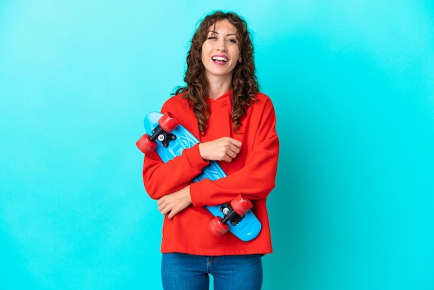 Young woman with curly hair isolated on blue background with a skate with happy expression