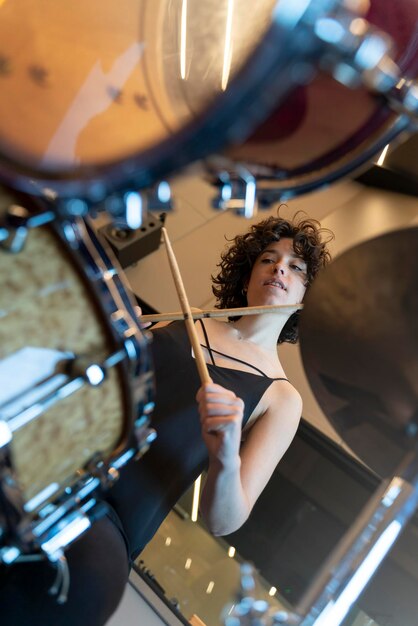 Young woman with curly hair playing the drums in a recording\
studio vertical photo