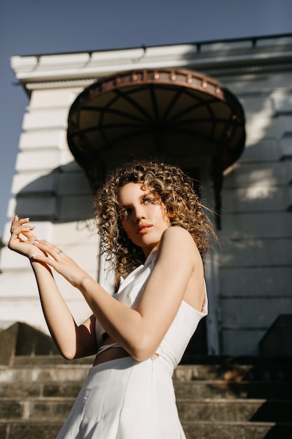 Young woman with curly hair posing in harsh light on a city building background