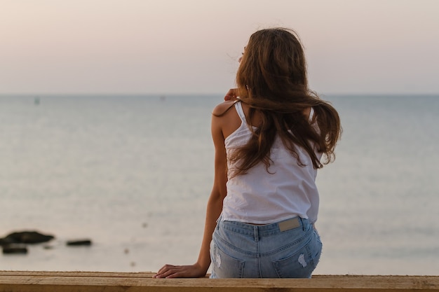 朝のビーチに座って、日の出を待つ巻き毛の若い女性