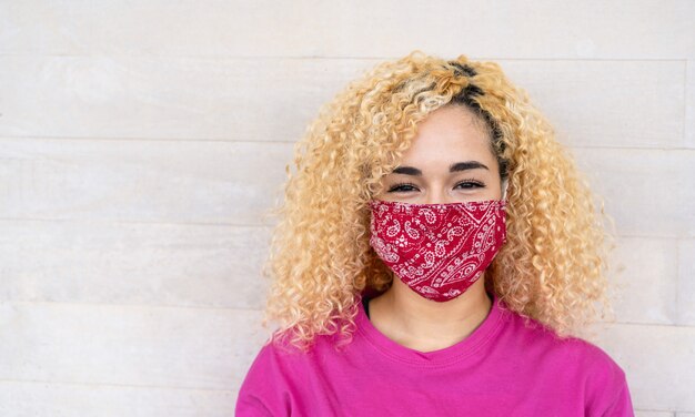 코로나 바이러스 발생 동안 얼굴 마스크를 착용하는 동안 곱슬 머리가 카메라 앞에서 웃고있는 젊은 여성