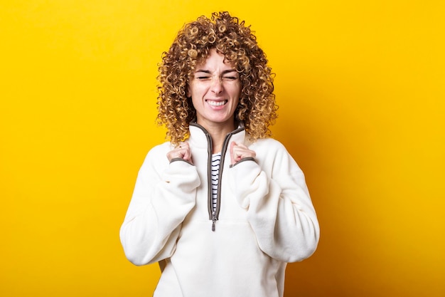 Young woman with curly hair squinting fists clenched on a yellow background