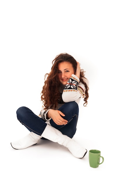 Young woman with Curly Hair in a Sweater and White Boots Sits with a Cup of Tea