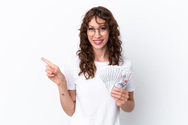 Young woman with curly hair taking a lot of money isolated background on white background pointing to the side to present a product