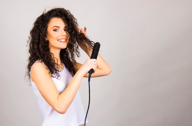 Young woman with curly hair with hair straightener