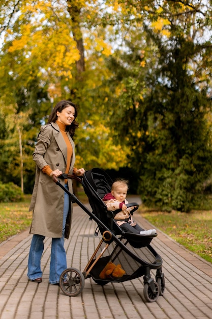 Young woman with cute baby girl in baby stroller at the autumn park