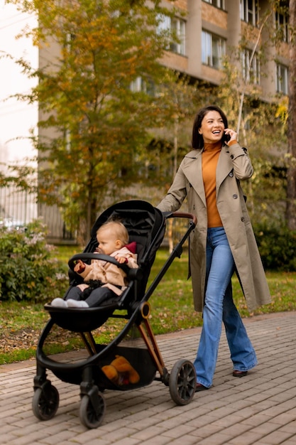 Foto giovane donna con una bambina carina in passeggino usando il telefono cellulare al parco d'autunno